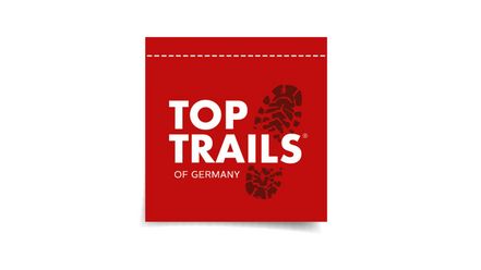 Logo mit weißer Schrift 'TOP TRAILS OF GERMANY' und schwarzem Schuhabdruck auf rotem Hintergrund